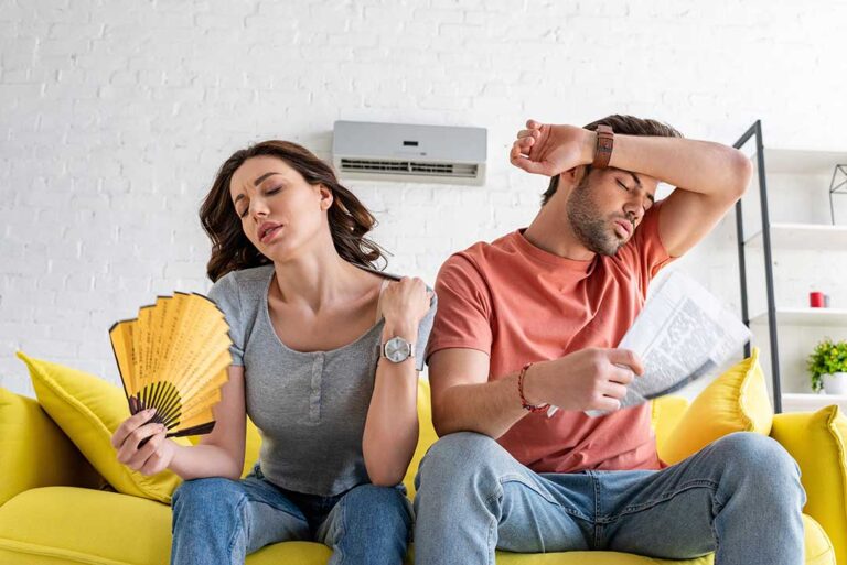 A person adjusting a digital thermostat in a modern living room with sunlight streaming through the window.
